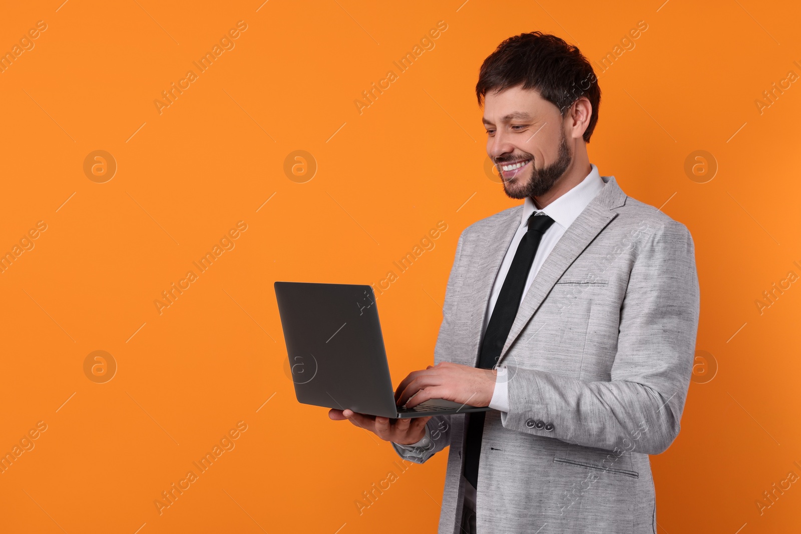 Photo of Happy man with laptop on orange background, space for text