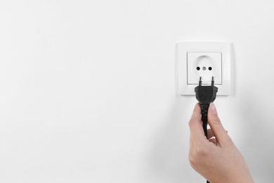 Photo of Woman putting plug into power socket on white background, closeup. Electrician's equipment