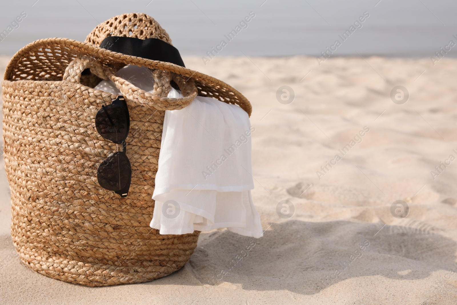 Photo of Beach bag, towel, sunglasses and hat on sandy seashore, space for text