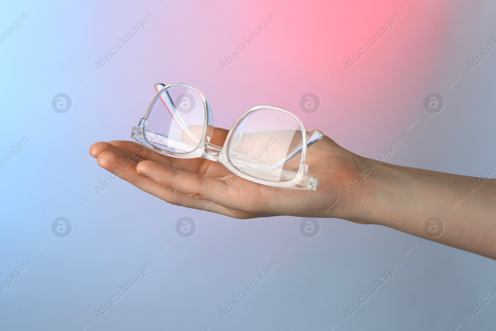 Photo of Woman holding glasses with transparent frame on color background, closeup