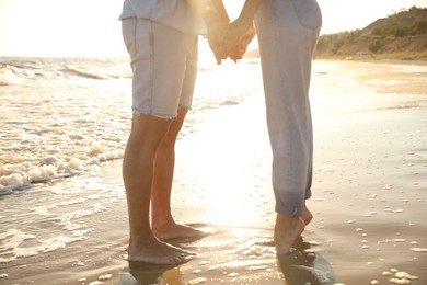 Couple on sandy beach near sea at sunset, closeup of legs