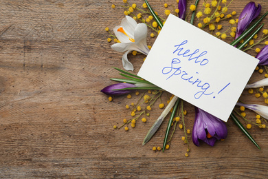 Photo of Card with words HELLO SPRING and fresh flowers on wooden table, flat lay. Space for text