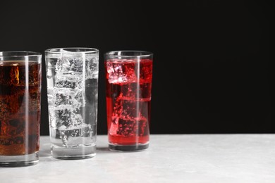 Photo of Glasses of different refreshing soda water with ice cubes on white marble table, space for text
