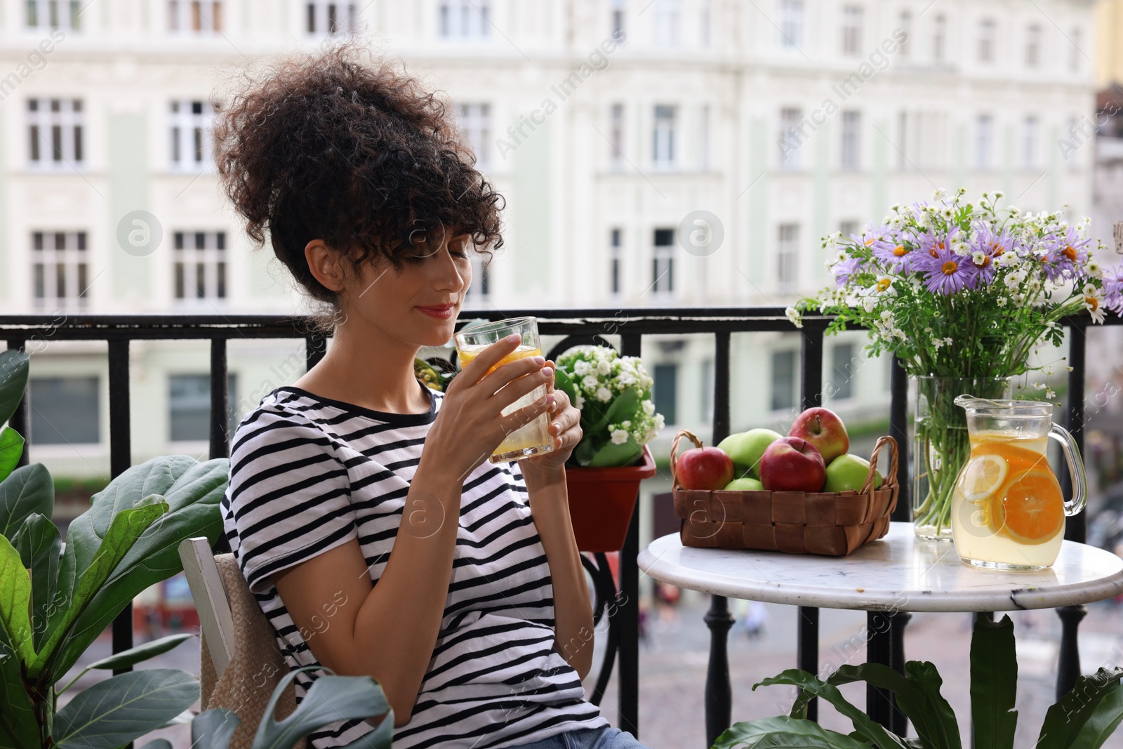 Photo of Young woman with glass of refreshing drink near beautiful houseplants on balcony