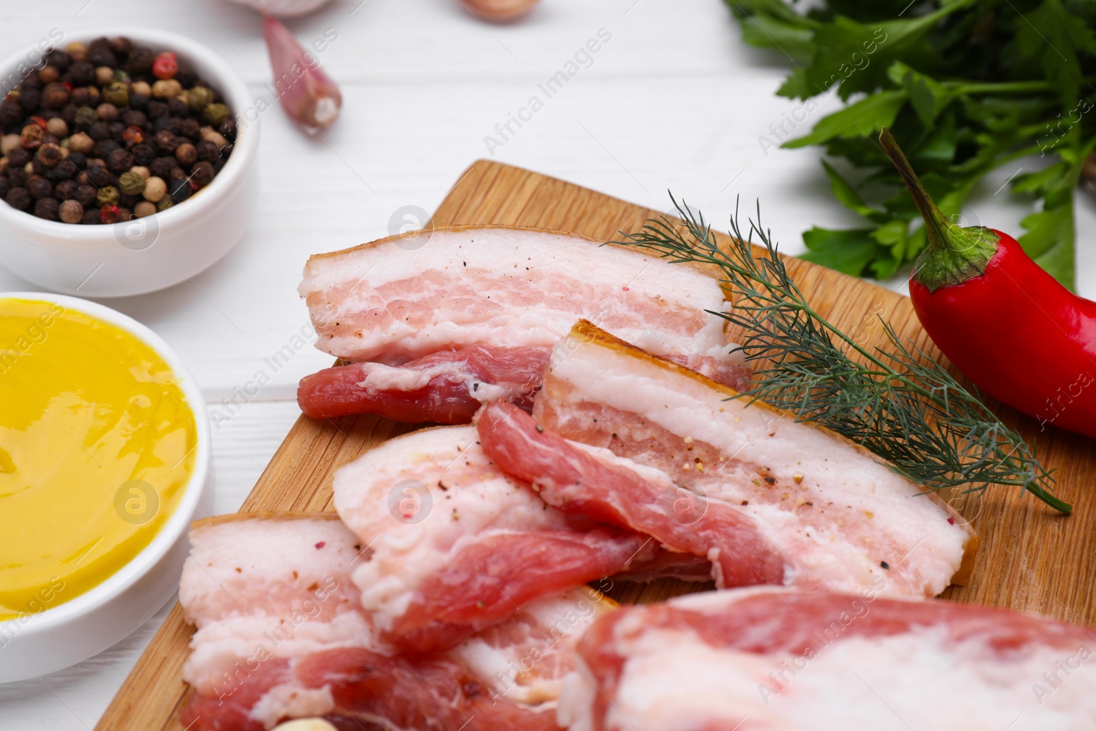 Photo of Slices of tasty pork fatback with dill, peppercorns and sauce on white table, closeup