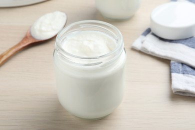 Photo of Glass jar with tasty yogurt on white wooden table, closeup