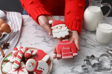 Woman holding delicious homemade Christmas cookies at white marble table, closeup