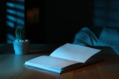 Open book and cactus on wooden table at night