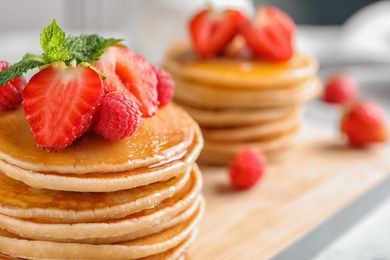 Photo of Tasty pancakes with berries and honey on wooden board, closeup