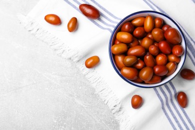 Photo of Fresh Ziziphus jujuba fruits with bowl and napkin on light table, flat lay. Space for text