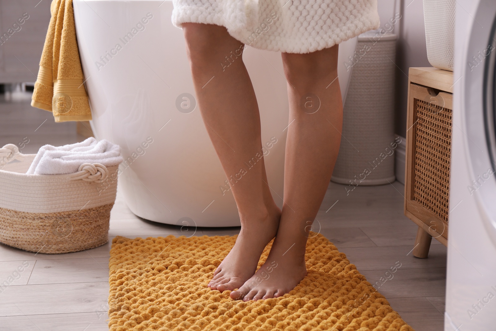 Photo of Woman standing on soft yellow bath mat near tub at home, closeup