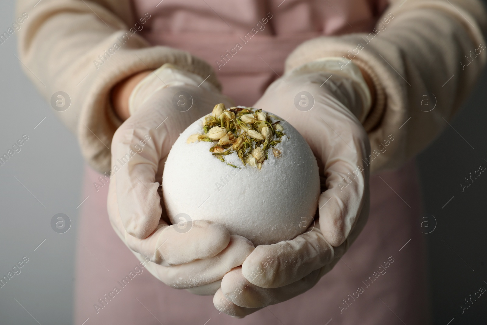 Photo of Woman in gloves with self made bath bomb on grey background, closeup