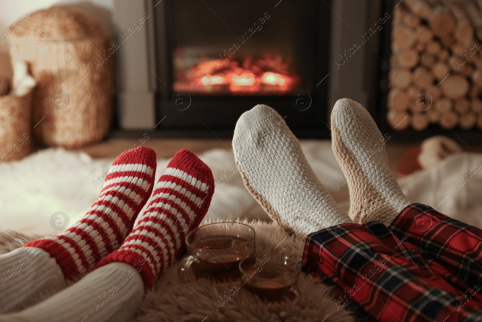 Photo of Couple in knitted socks near fireplace at home, closeup of legs