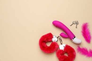 Vaginal vibrator, feathers and handcuffs on beige background, flat lay with space for text. Sex toys