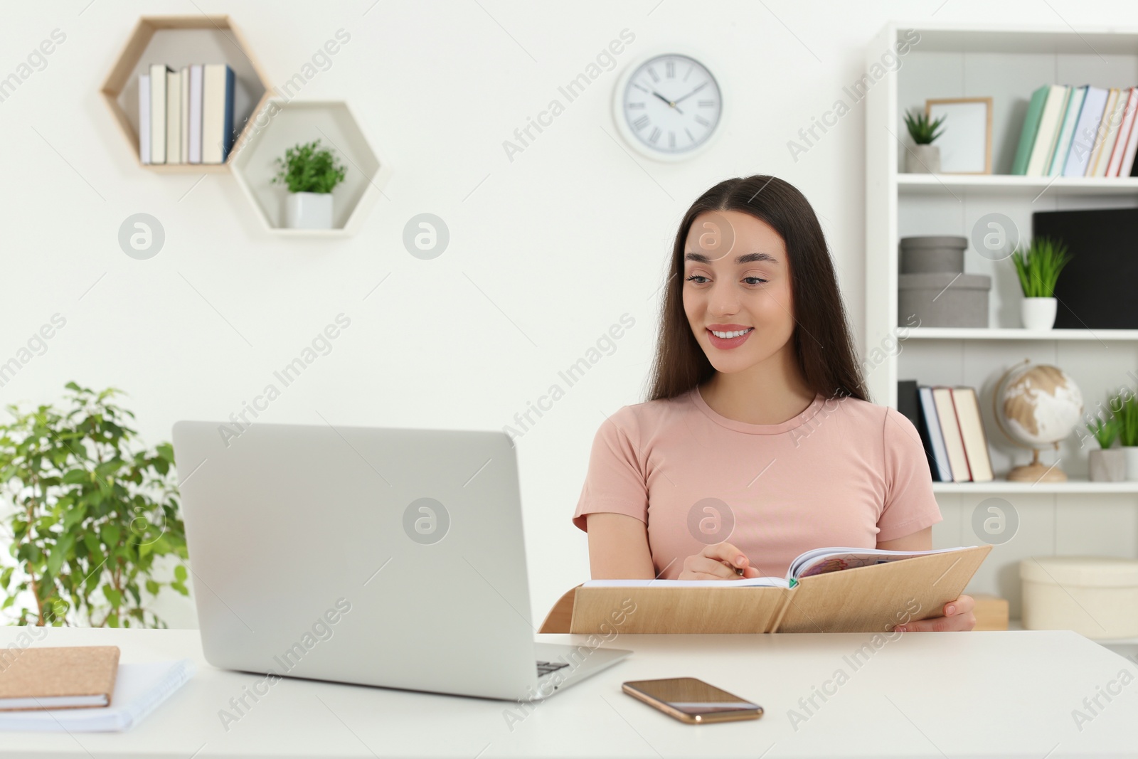 Photo of Home workplace. Happy woman writing in notebook at white desk in room