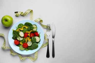Measuring tape, salad, apple and cutlery on light background, flat lay. Space for text