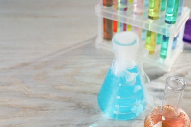 Laboratory glassware with colorful liquids and steam on white wooden table, space for text. Chemical reaction