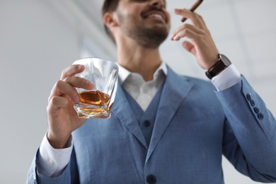Photo of Man with glass of whiskey and cigar indoors, closeup