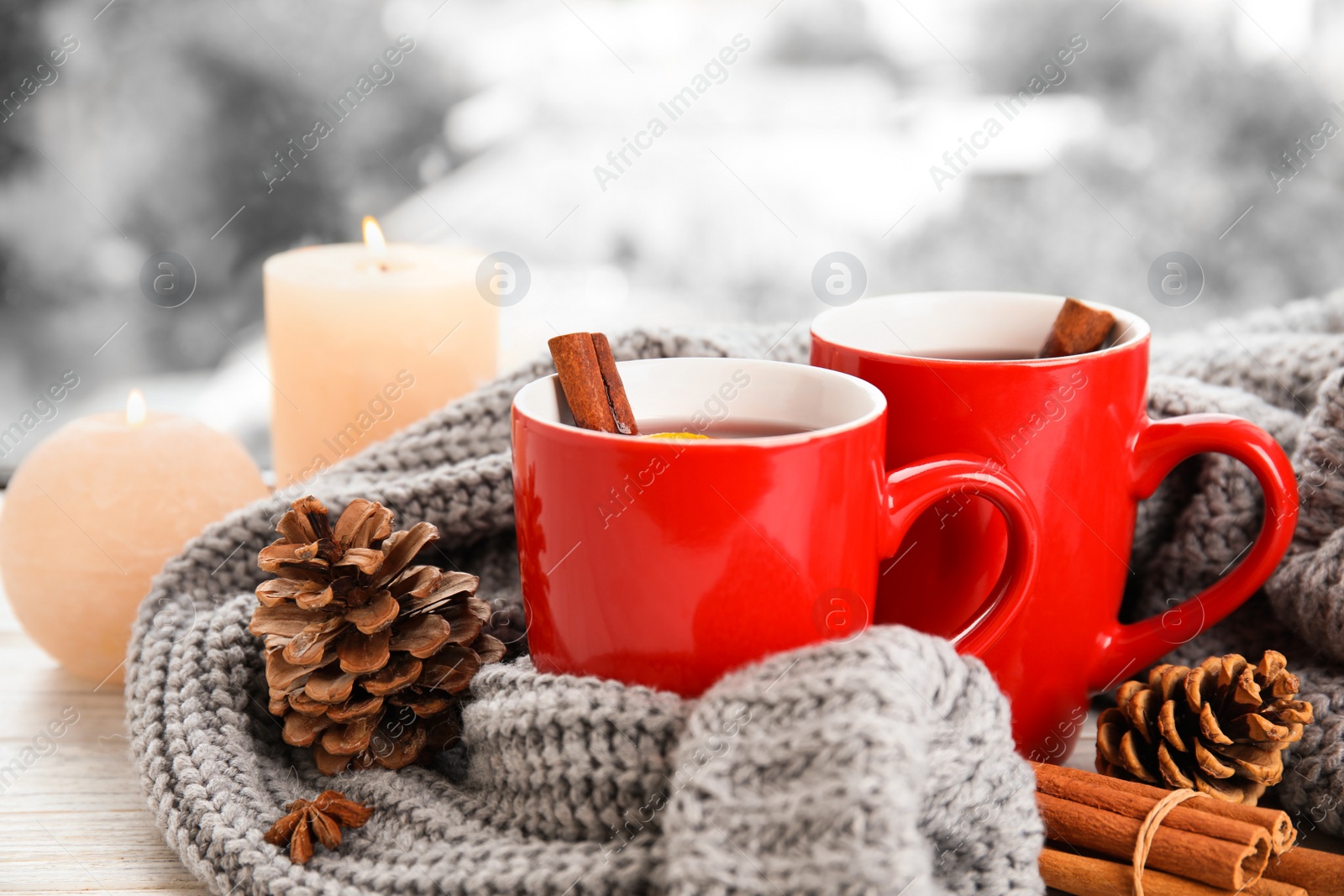 Photo of Cups of hot winter drink with knitted sweater on window sill indoors