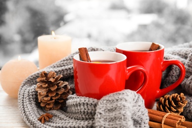 Photo of Cups of hot winter drink with knitted sweater on window sill indoors