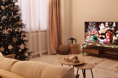 Wide TV set, furniture, snacks and Christmas tree in stylish room