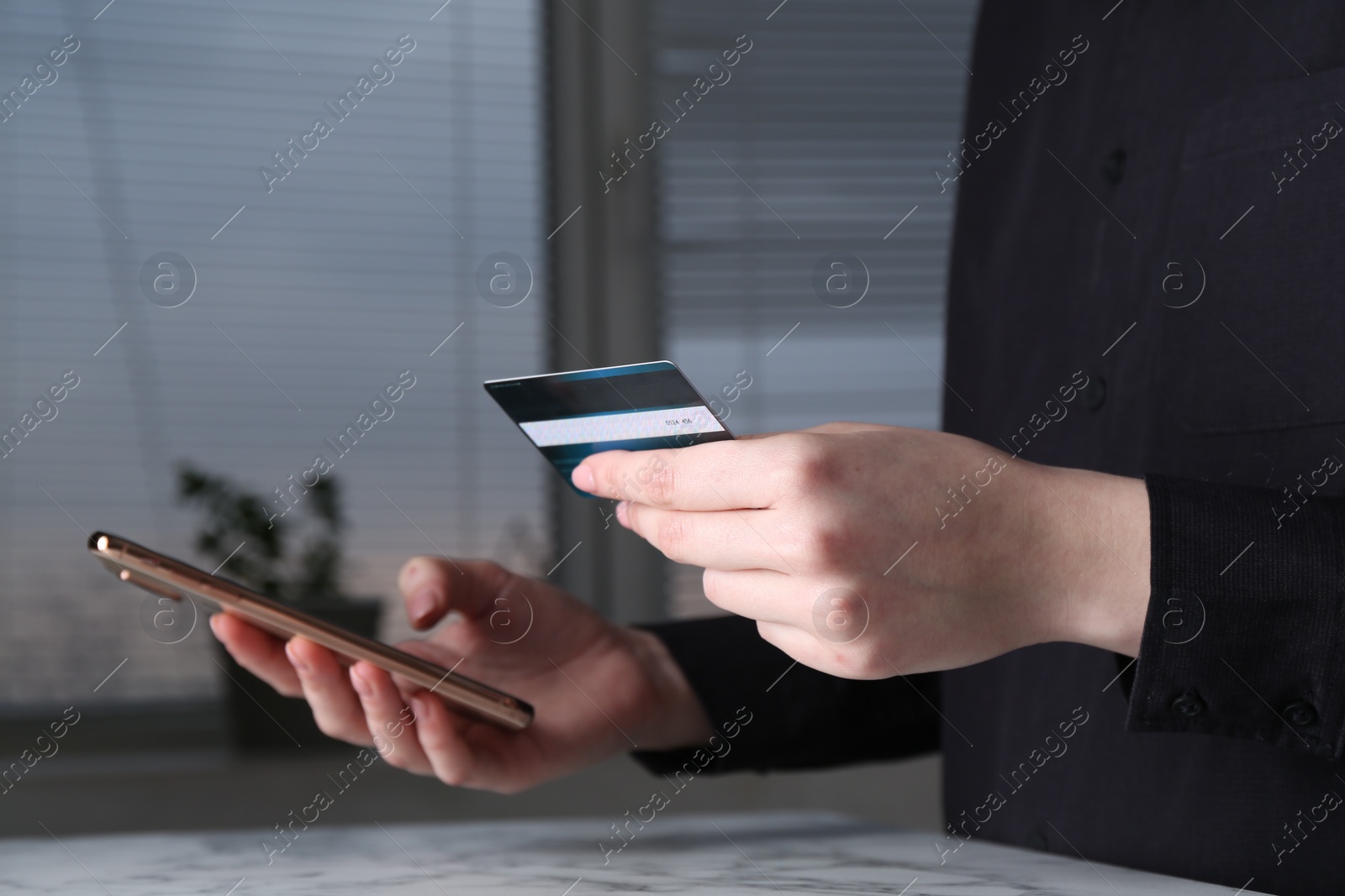 Photo of Online payment. Woman with smartphone and credit card at white marble table indoors, closeup