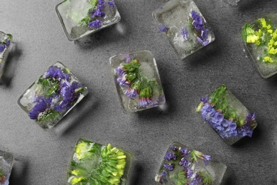 Ice cubes with flowers on grey stone background, flat lay