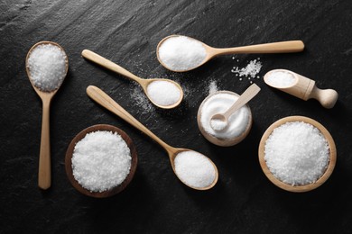 Organic white salt in bowls and spoons on black table, flat lay