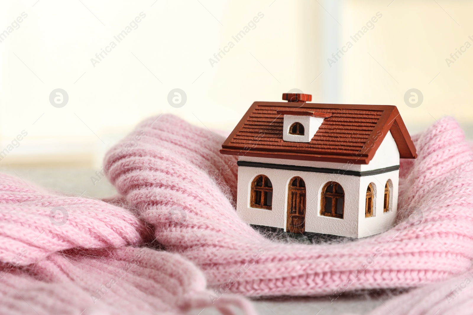 Photo of House model and pink scarf on table on blurred background, space for text. Heating efficiency