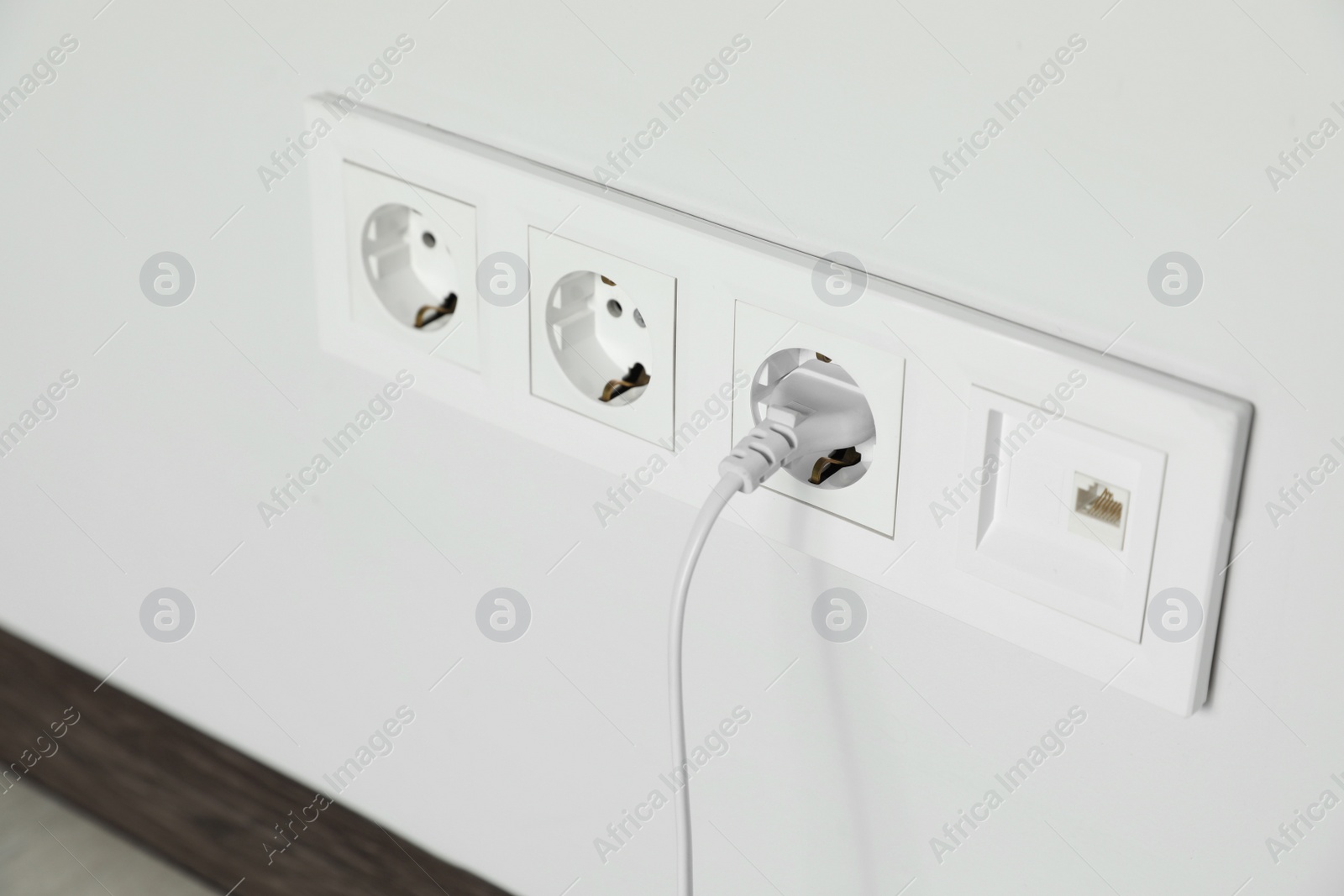Photo of Power sockets with inserted plug on white wall indoors, closeup. Electrical supply