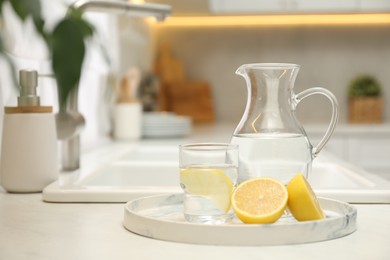 Photo of Jug, glass with clear water and lemons on white table in kitchen, space for text