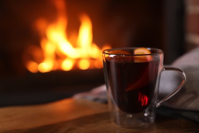 Tasty mulled wine, plaid and blurred fireplace on background