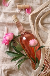 Flat lay composition with rose wine, mesh bag and beautiful peonies on white fabric