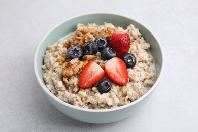 Photo of Tasty oatmeal with strawberries, blueberries and walnuts in bowl on grey table