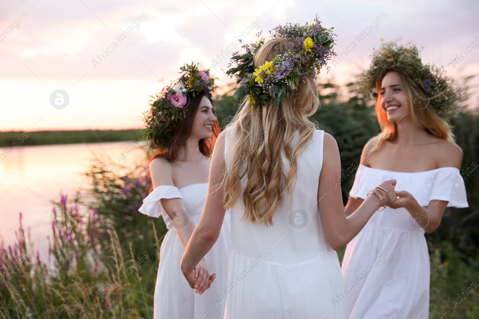 Photo of Young women wearing wreaths made of beautiful flowers outdoors at sunset