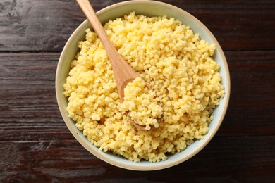 Tasty millet porridge and spoon in bowl on wooden table, top view