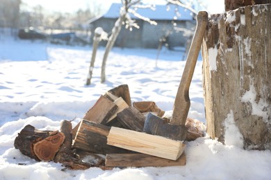 Photo of Metal axe and pile of wooden logs outdoors on sunny winter day