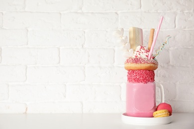 Tasty milk shake with sweets in mason jar served on table near brick wall. Space for text