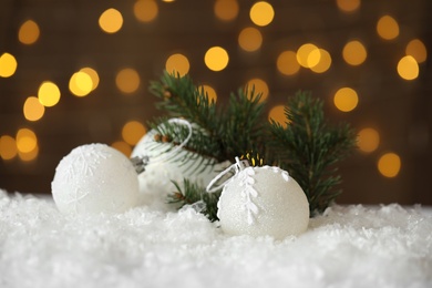 Photo of Beautiful Christmas balls and fir branch on snow against blurred festive lights