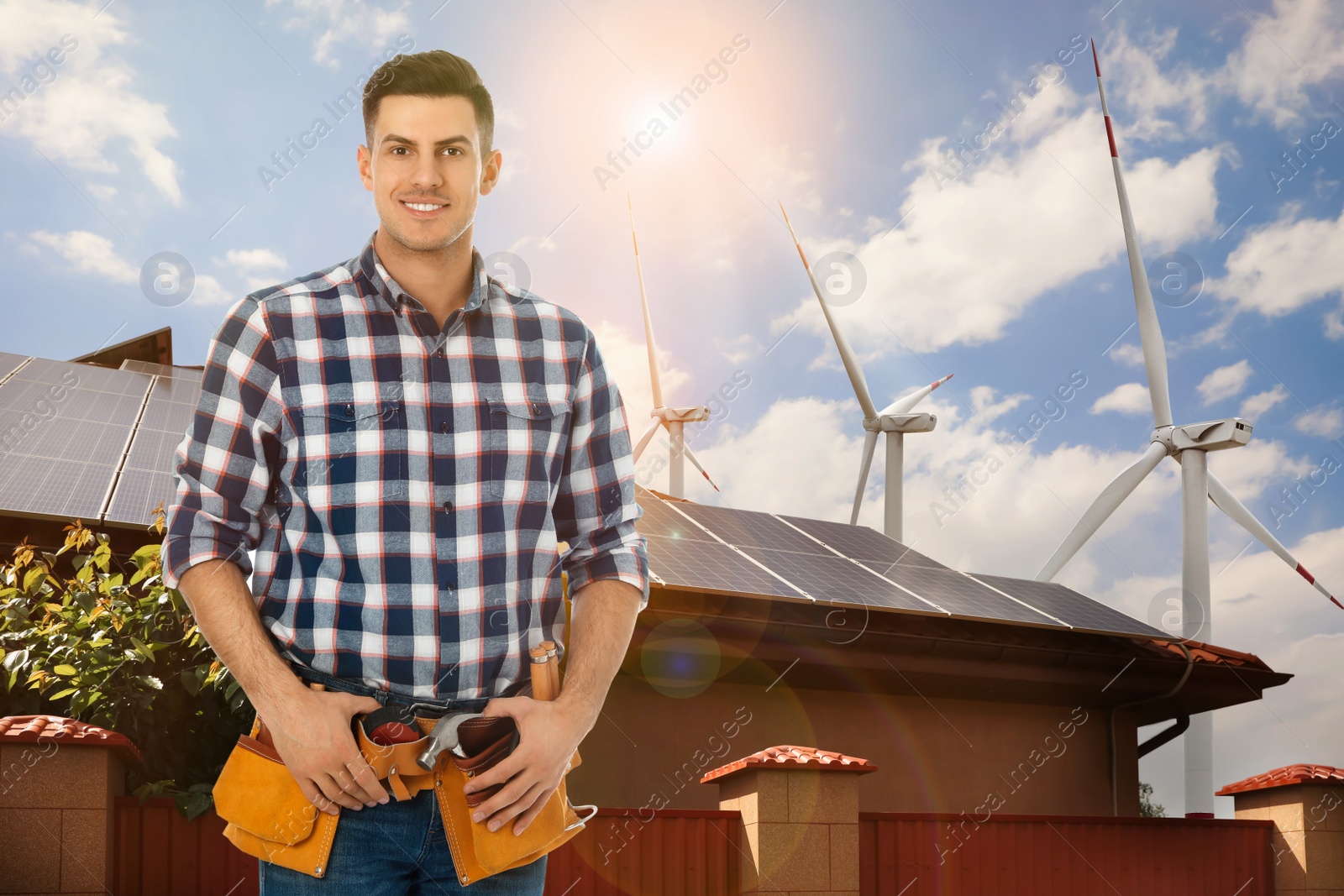 Image of Worker with tool belt and view of wind energy turbines near house with installed solar panels on roof