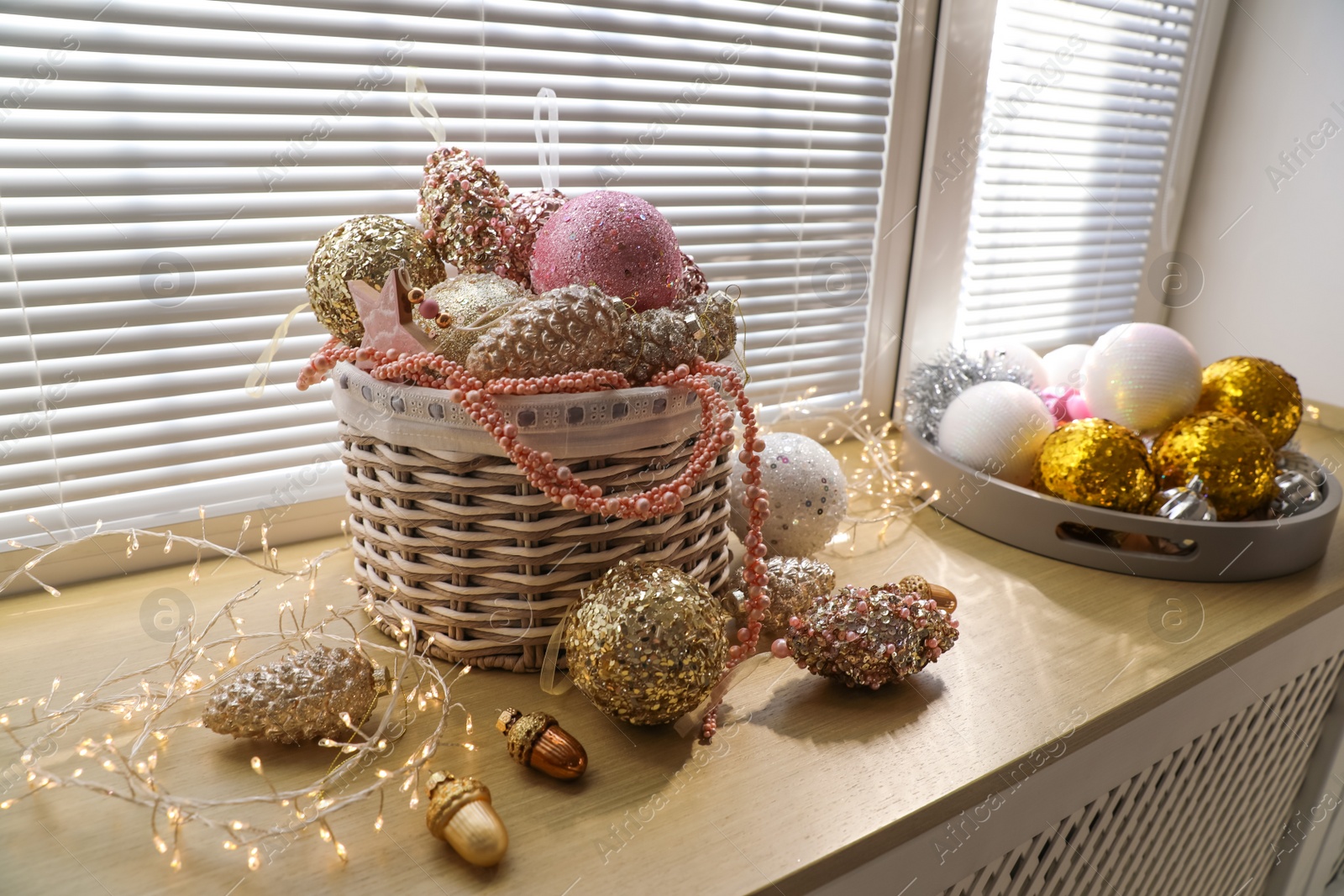 Photo of Basket with beautiful Christmas tree baubles and fairy lights on window sill indoors