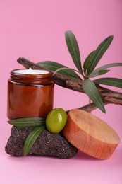 Photo of Jar of cream with olive essential oil on stone against pink background
