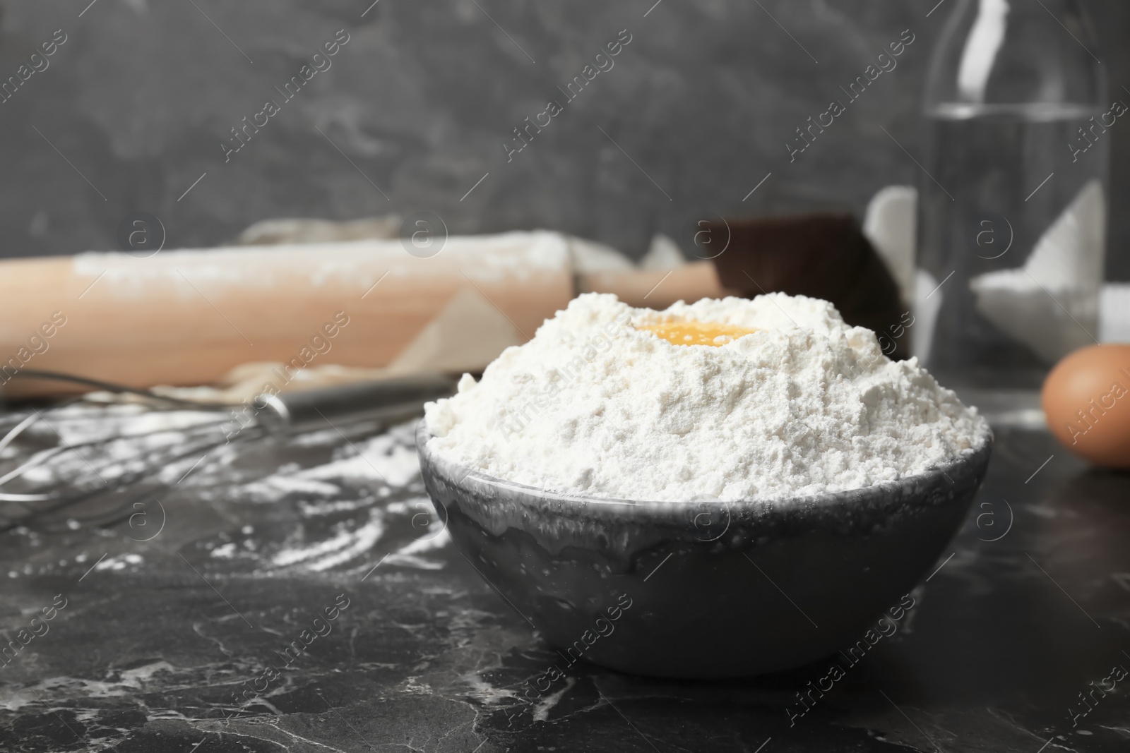 Photo of Bowl with flour and egg on table