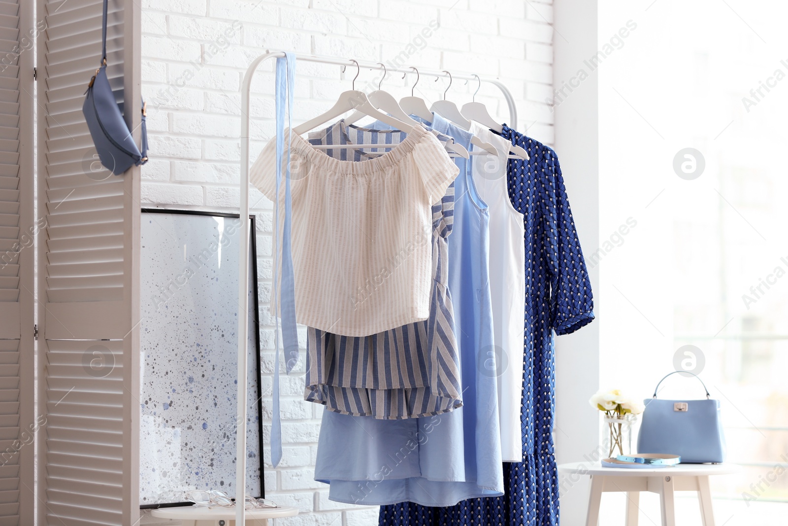 Photo of Wardrobe rack with women's clothes at white brick wall in room