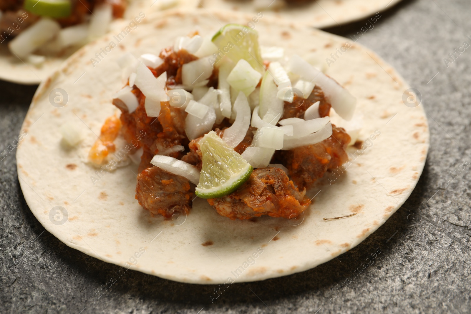 Photo of Delicious tacos with vegetables, meat and lime on grey textured table, closeup