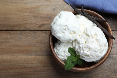 Photo of Yummy vanilla ice cream in bowl on wooden table, flat lay. Space for text