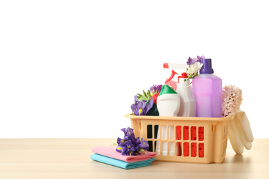 Photo of Plastic basket with spring flowers and cleaning supplies on wooden table. Space for text