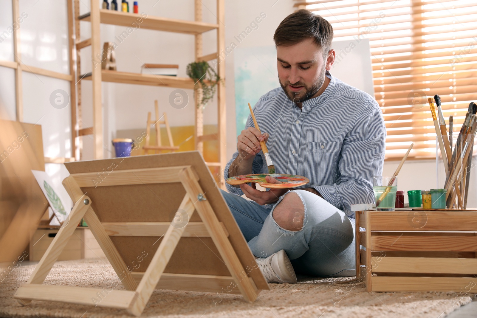 Photo of Young man painting on easel with brush in artist studio