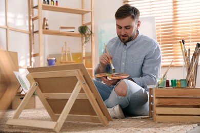 Photo of Young man painting on easel with brush in artist studio