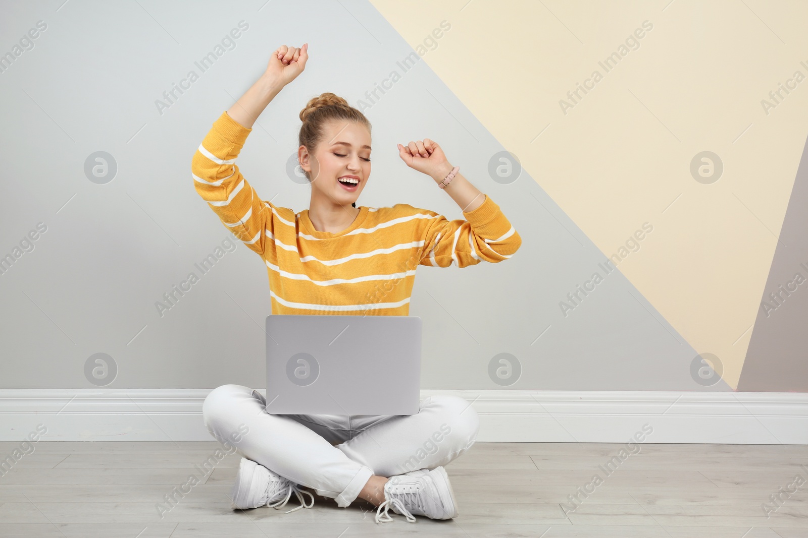 Photo of Emotional young woman with laptop on floor near color wall. Space for text